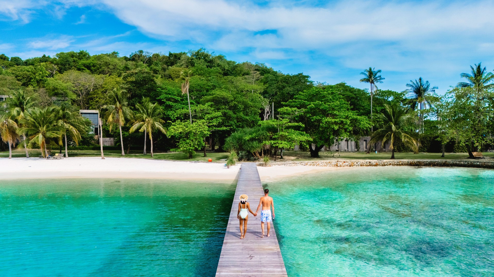 Couple walking hand in hand along the wooden pier at a tropical beach in the sunny afternoon
